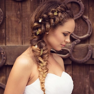 Detail of golden dreadlock charms with leaf and shell pendants on braided hair