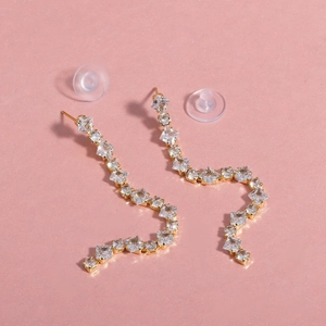Sparkling gold S-shaped fringe earrings with square crystals on a pink background
