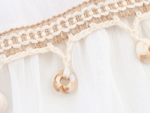 Close-up of white pleated fabric with woven lace trim and seashell bead decorations