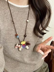 Detail view of handmade embroidered pony pendant necklace on warm brown knit sweater