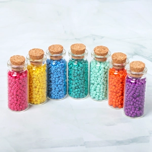 Perline colorate in vetro da 3mm in otto bottiglie di vetro su superficie di marmo