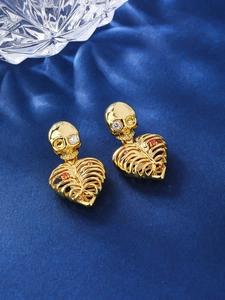 Macro shot of gold gothic skull and heart rib cage earrings on blue velvet fabric