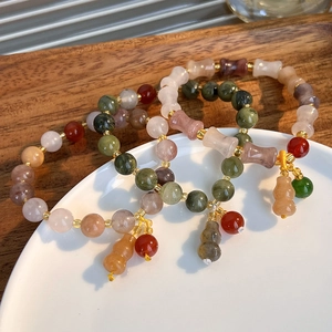 Detailed close-up of multi-color stone bead bracelets with jade gourd charm on a ceramic tray