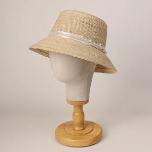 Beige straw sun hat with white lace ribbon and pearl accents on a wooden stand