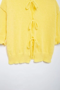 Detail of yellow knit cardigan featuring three delicate back ribbon bow ties and ruffle trim