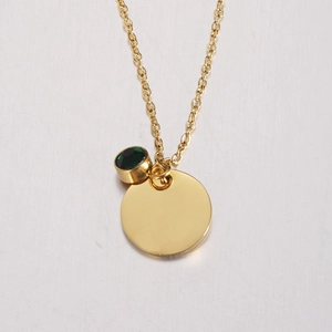 Close-up of golden necklace with a polished round pendant and a green gemstone
