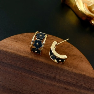 Detailed shot of gold C-shaped flower earrings with black enamel on a wooden stand