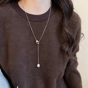 Detail of a gold Y-shaped necklace with irregular pearl pendant on a brown sweater