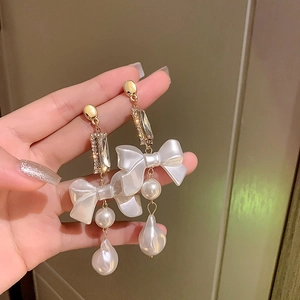 Detailed view of long bowknot earrings with pearls and crystals held by a hand