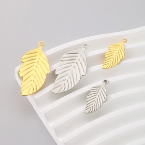 Detailed view of gold and silver hollow leaf charms on a textured white display stand