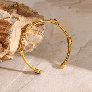 18K gold plated stainless steel bangle with green gemstone on rustic stone base
