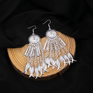 Macro detail of silver tassel earrings with fish charms on wooden and silk background