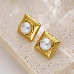 Macro shot of square gold earrings with white pearl inlay on textured stone