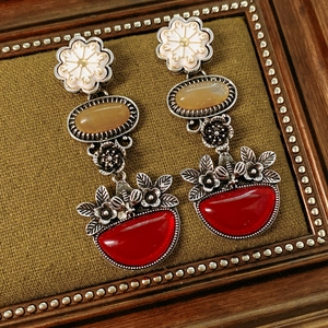 Detail of vintage flower earrings with red and amber stones on green textured fabric