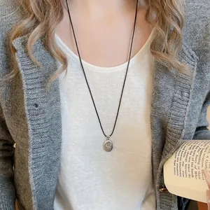 Minimalist silver swirl pendant necklace with black wax cord on a model's neck