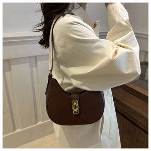 Detail view of dark brown leather crescent bag with gold ring buckle worn with beige coat