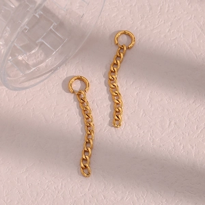 Détail de boucles d'oreilles chaîne Figaro dorées sur un fond rose texturé