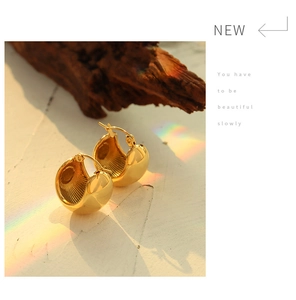 Detail of gold bulbous C-shape earrings with vertical stripe interior textures