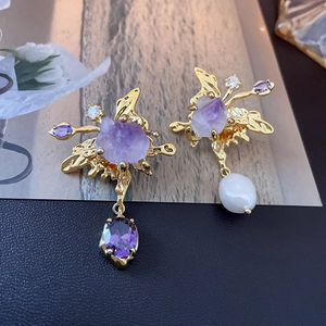 Detailed macro of asymmetric gold earrings with purple amethyst and baroque freshwater pearl