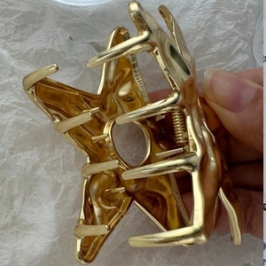 Golden hollow star metal claw clip held by hand showing minimalist polished hair accessory