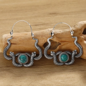 Detailed view of silver snake-shaped earrings with turquoise stones on a wood surface