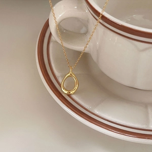 Macro view of gold teardrop hollow pendant on a minimalist necklace draped over a ceramic cup