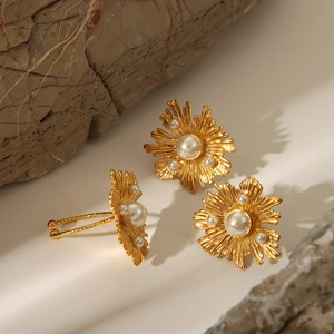 Detailed macro view of gold flower earrings set with faux pearls on natural stone background