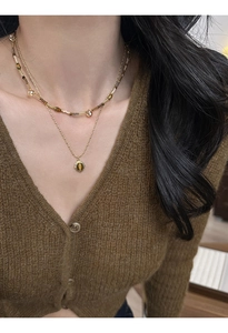 Close-up of double-layered gold necklace with brown oval tiger eye pendant on a model