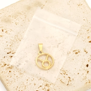 Macro detail of golden stainless steel Taurus zodiac pendant on beige stone surface
