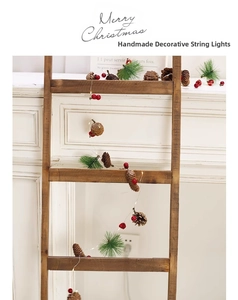 Close-up of Christmas pine cone string lights with red berries on a rustic wooden ladder