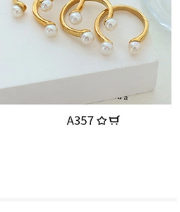 Detail shot of gold-plated open rings featuring elegant white pearls on a tiered stand