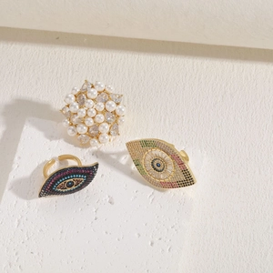 Three gold rings featuring white pearl and evil eye designs with colorful gemstones