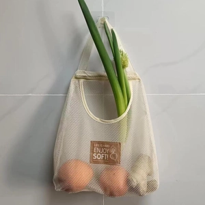 Macro detail of breathable mesh storage bag holding fresh onions and ginger on a tiled wall