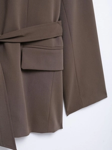 Close-up of brown blazer featuring a flap pocket and adjustable waist tie belt detail