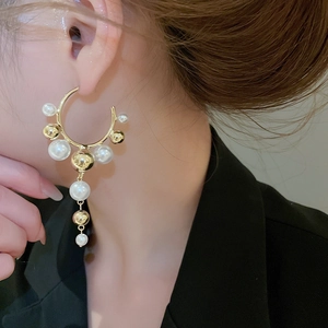 Close-up of elegant gold C-shaped earrings with pearl tassels worn by a model