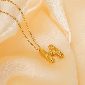 Modern gold lava textured letter H pendant necklace on elegant silk background