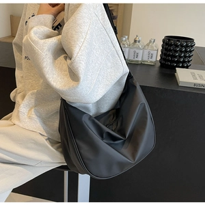 Close-up of a black crescent nylon crossbody bag on a model in a modern café setting