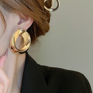 Close-up of golden geometric rotating hoop earrings worn by a model in soft lighting