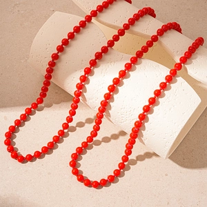 Detail of elegant long red pearl beaded necklace draped on white geometric props