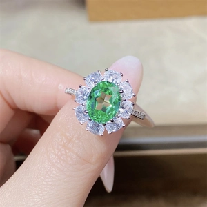 Macro detail of silver ring featuring a large green oval gemstone and floral halo setting