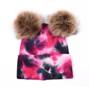Détail d'un bonnet en tricot tie-dye rose avec deux grands pompons en fourrure marron