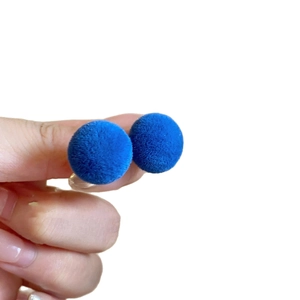 Blue flocked spherical stud earrings with a velvet texture held against a white background