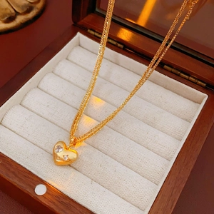 Gros plan du collier double cœur doré avec pierres précieuses dans un écrin en bois
