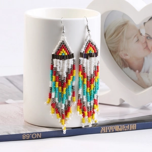 Ethnic style long beaded tassel earrings in vibrant colors hanging on a white ceramic mug