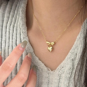 Close-up of a gold bow and heart pendant necklace worn on a soft knit sweater