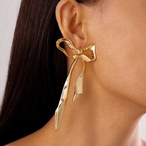 Gros plan d'un mannequin portant de grandes boucles d'oreilles nœud en métal doré poli