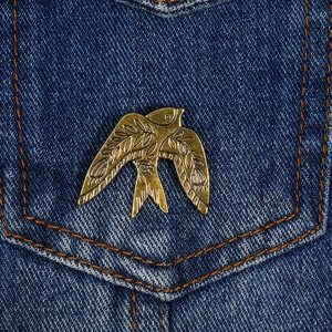 Gros plan d'une broche oiseau en métal doré avec gravure florale sur du denim bleu