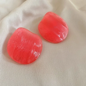 Macro detail of irregular orange-pink resin earrings with a unique brushed texture