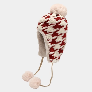 Close-up detail of red and white houndstooth winter trapper hat with soft pink faux fur pom poms