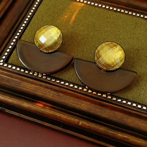Close-up of golden geometric earrings with dark brown resin charms on vintage stand